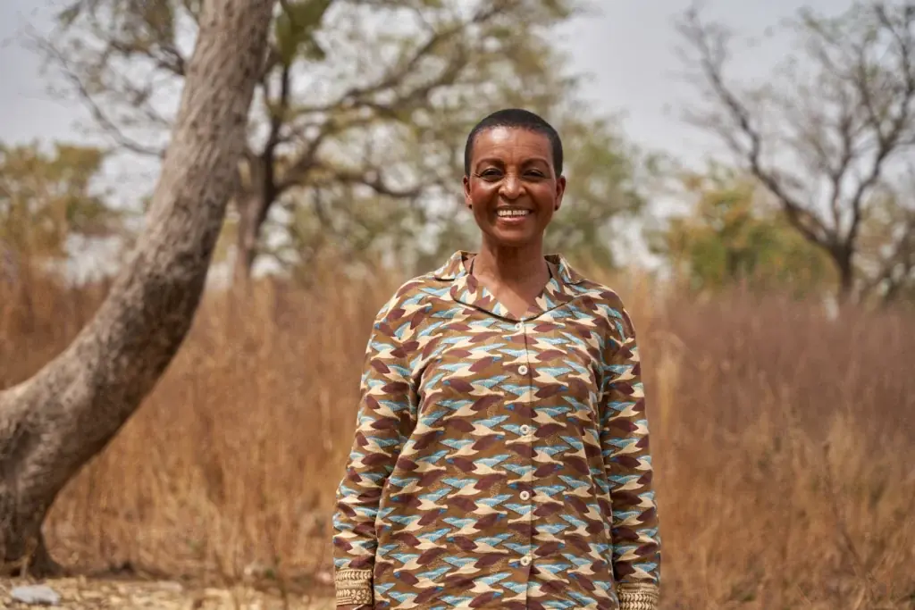Adjoa Andoh wearing a patterned shirt, standing in front of dry grassland and smiling.