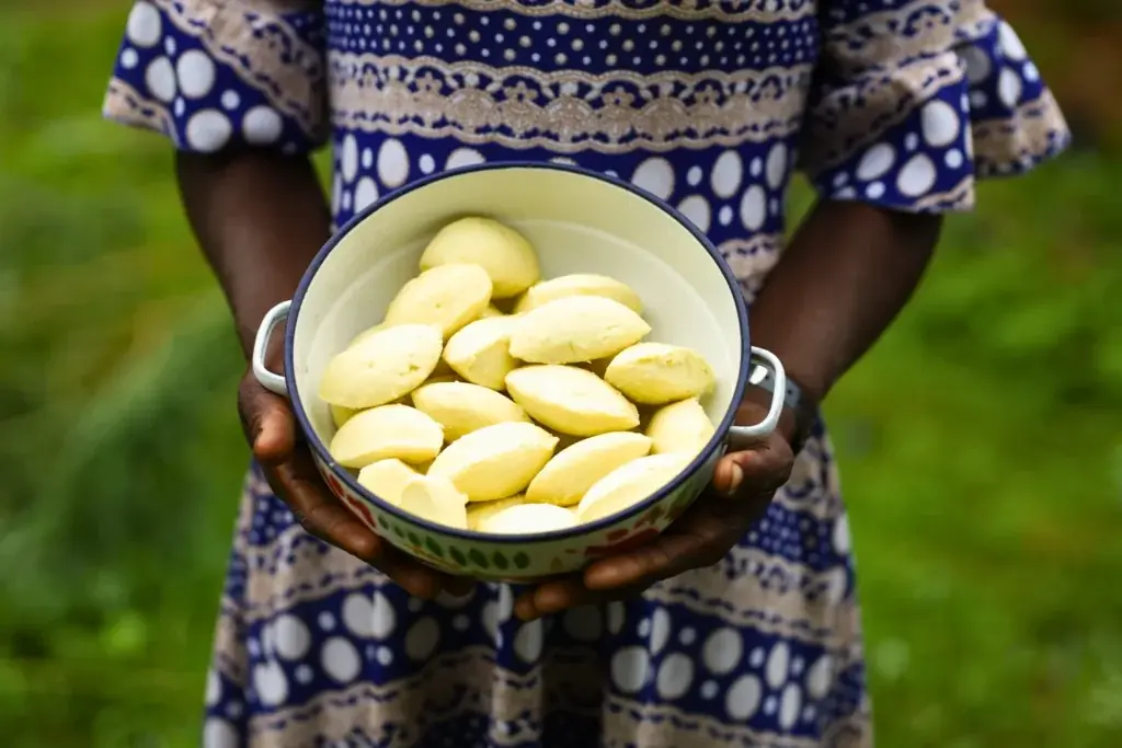 Person holding a bowl filled with freshly prepared shea butter outdoors.